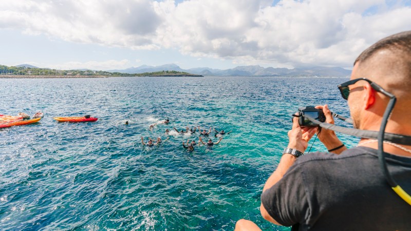 Man photographing people swimming near kayaks in the sea on a sunny day.