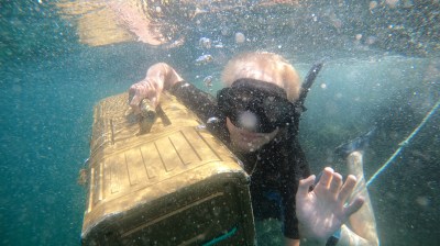 Person underwater holding a large golden case, wearing snorkeling gear.