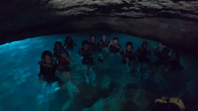 Group of people swimming in a dimly lit cave with blue water.