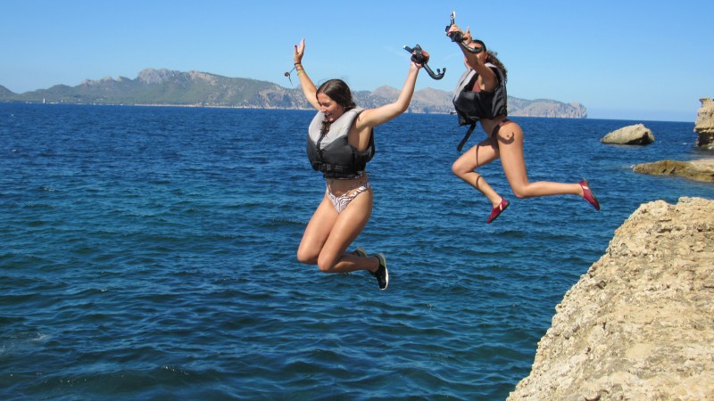 Two women in life vests cliff jumping into the sea.