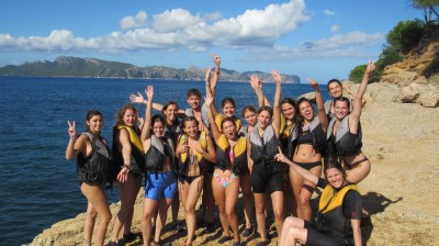 Group of people in life jackets posing on a rocky shore with the ocean in the background.