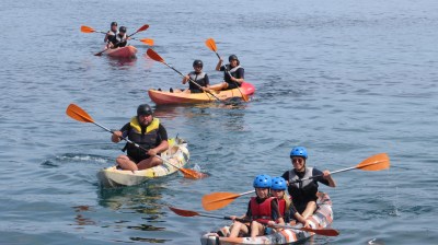 Group kayaking on the ocean, wearing life vests and helmets, with orange paddles.