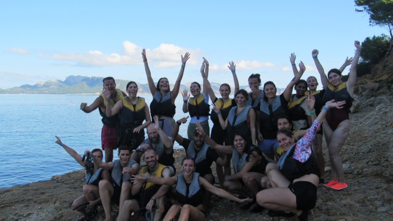 Group of people in life vests posing near a lakeside.