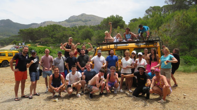 Group of people posing in front of a yellow vehicle with mountains in the background.