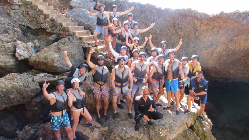 Group of people wearing helmets and life jackets posing on rocky terrain.