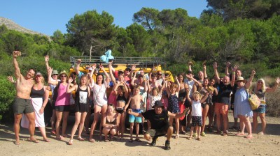 Group of people posing outdoors with a yellow jeep in a forested area.