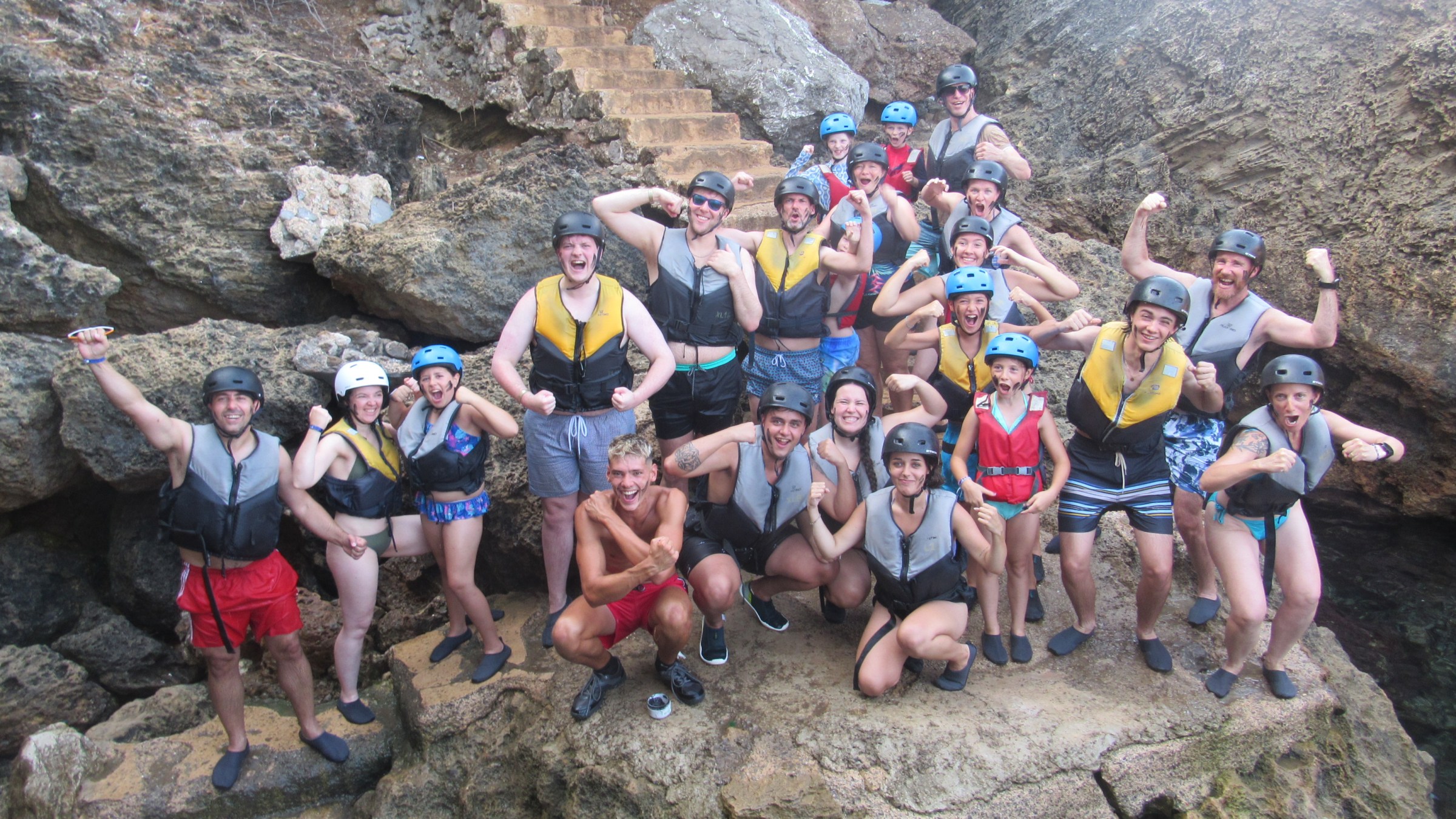 Group of people in life vests and helmets posing on rocks.