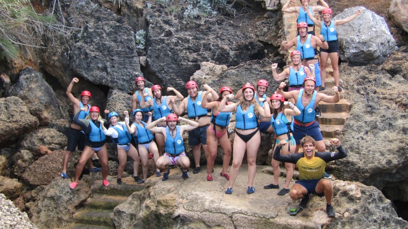 Group of people in helmets and life vests posing on rocky terrain.