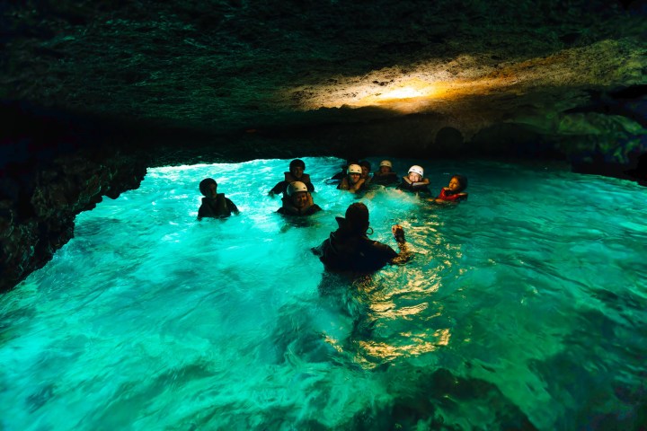 Group of people swimming in a turquoise-lit cave pool.