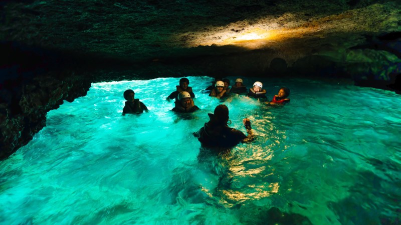 Group of people swimming in a turquoise-lit cave pool.