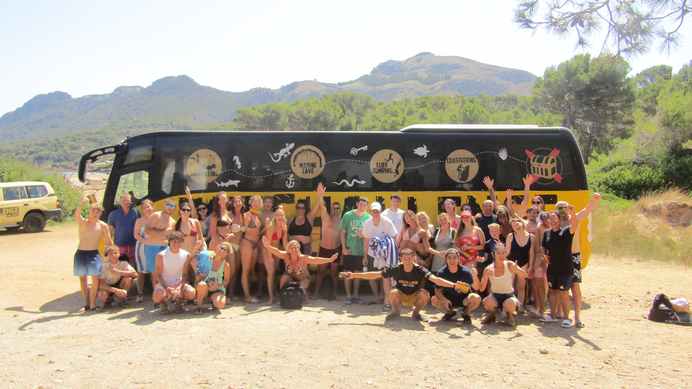 Group of people posing in front of a tour bus with mountains in the background.