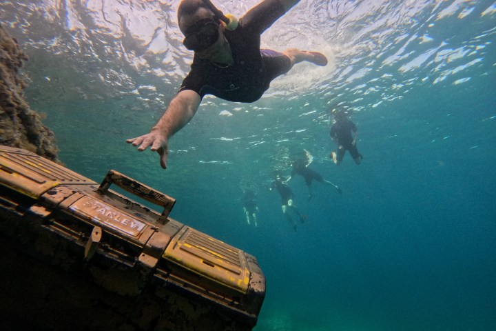 Snorkeler reaching for a submerged treasure chest underwater.