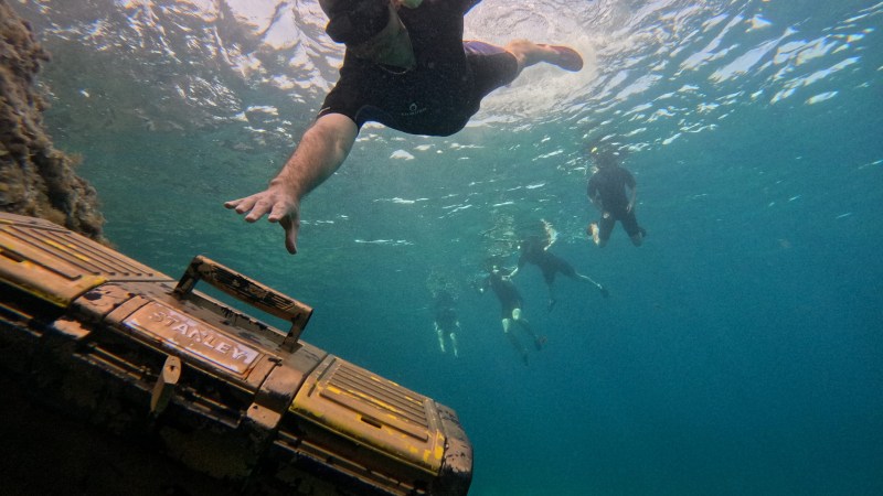 Snorkeler reaching for a submerged treasure chest underwater.